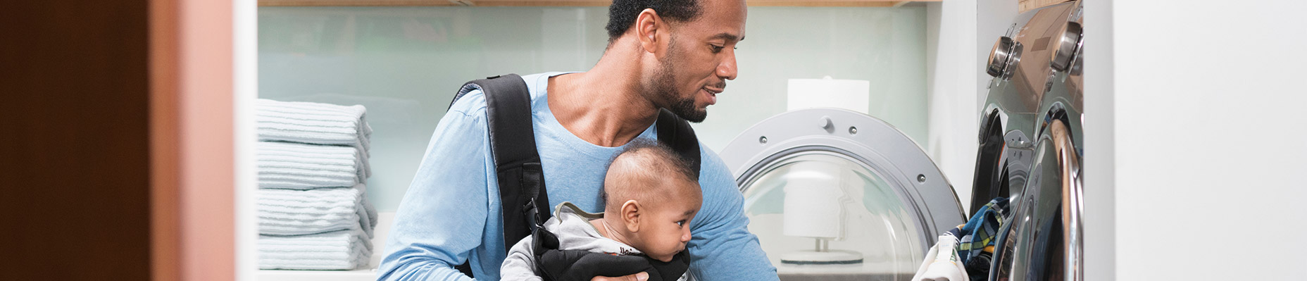 father with baby in harness loading laundry