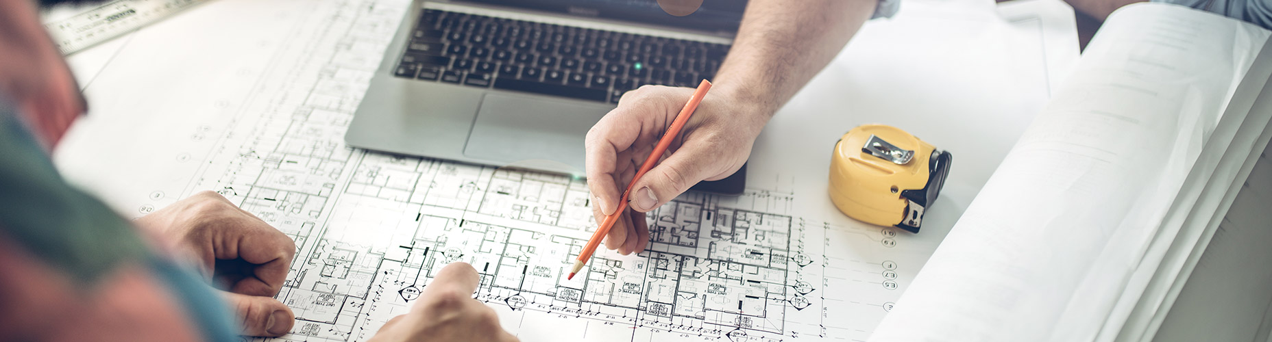 two hands over blueprint of home with measuring tape and pencil nearby